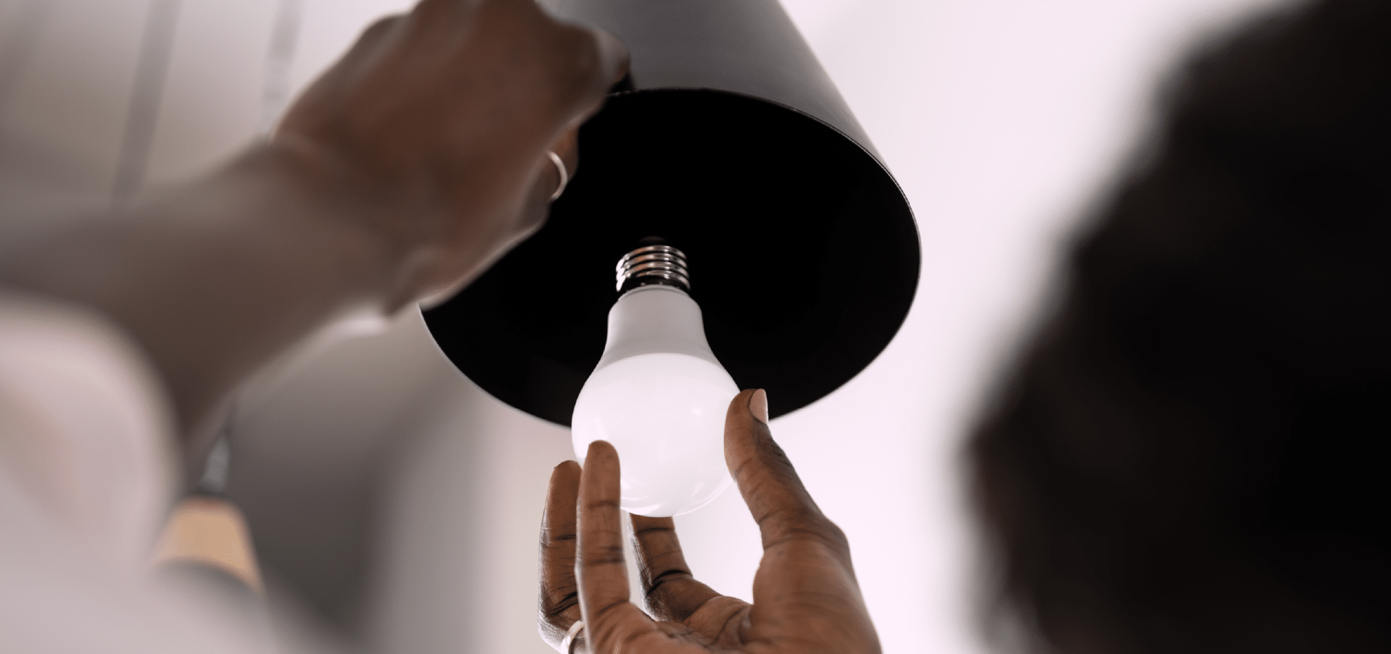 Close-up photo of two hands installing a white LED light bulb into a modern black lamp.